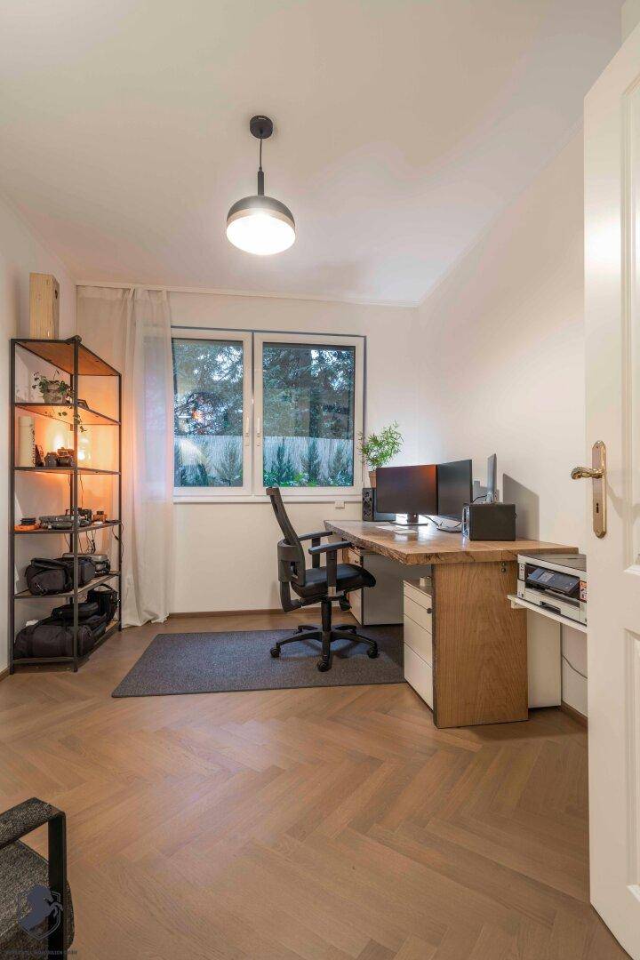 Helles Arbeitszimmer mit Schreibtisch, Regalsystem und Blick ins Grüne.
