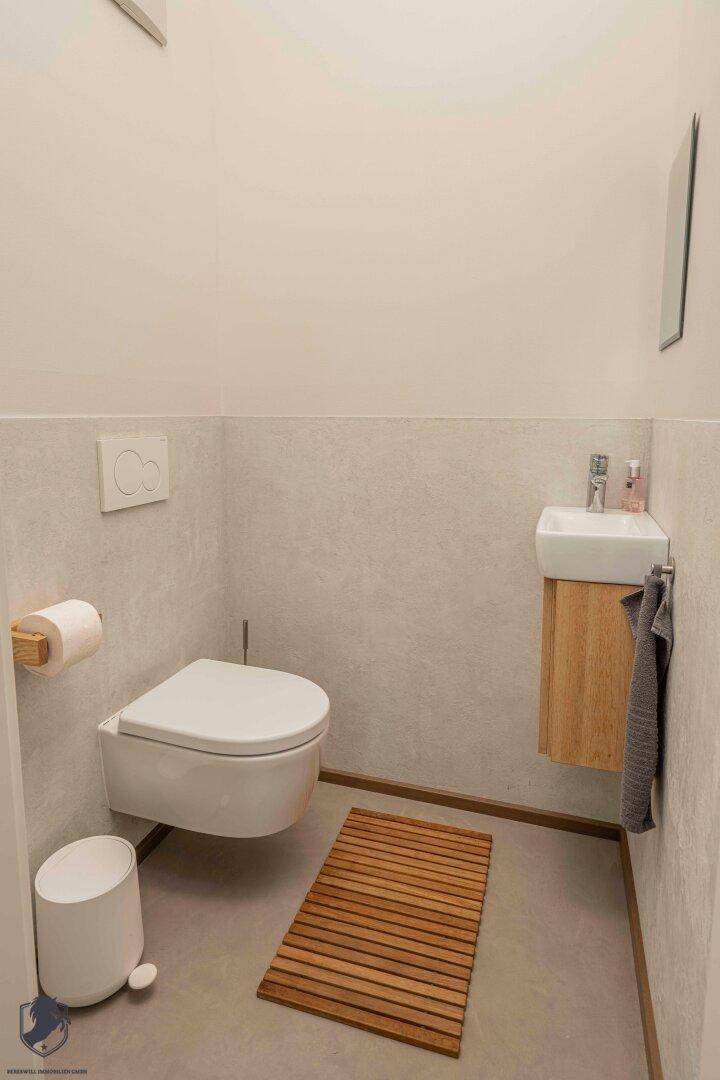 Helles Gäste-WC mit Wand-WC, kleinem Waschbecken und Holzakzenten.
