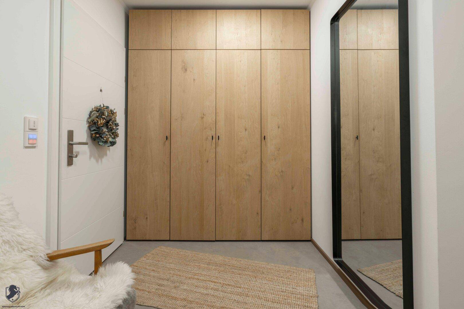 Eingangsbereich mit praktischen Einbauschränken aus Holz und großem Spiegel.