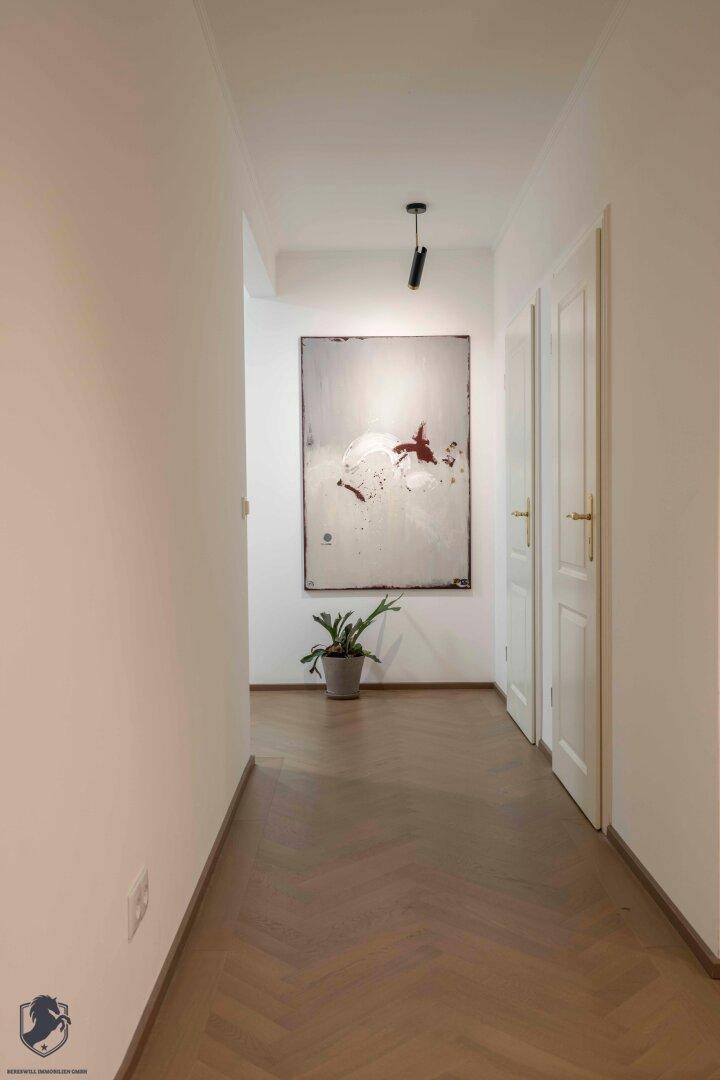 Heller Flur mit modernem Kunstwerk, Zimmerpflanze und Fischgrätparkett.