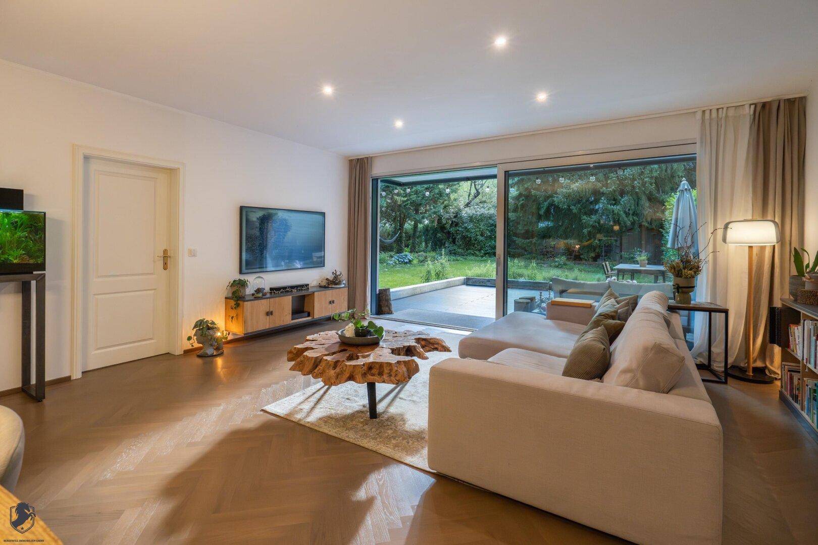 Helles Wohnzimmer mit bequemer Couch, Holzboden und großem Fenster zum Garten.