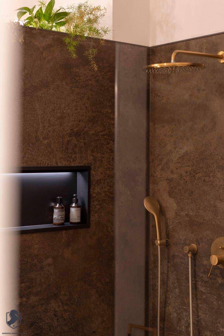 Moderne Dusche mit dunklen Fliesen, goldfarbenen Armaturen und integrierter Nische.