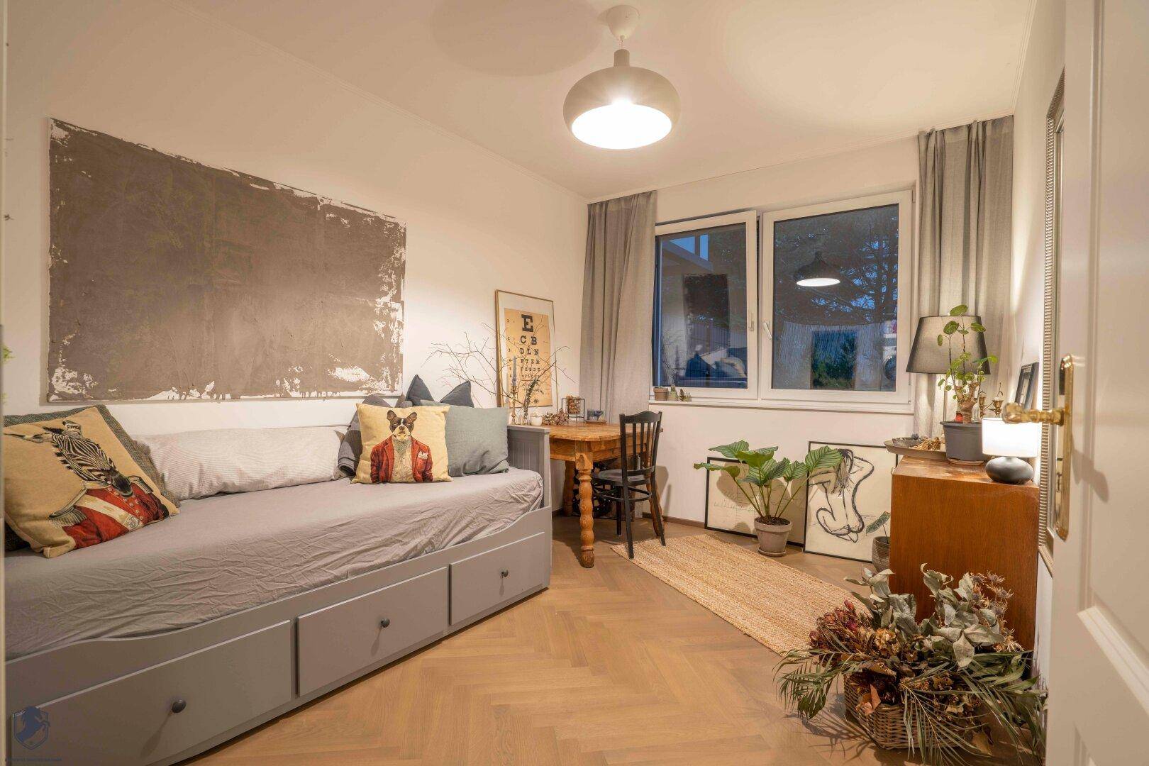 Gemütliches Schlafzimmer mit Tagesbett, Holzboden und Fenster mit Blick nach draußen.
