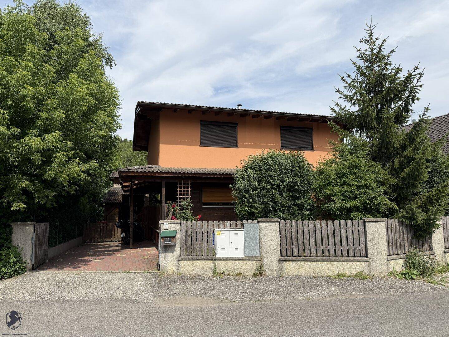 Ansicht des Wohnhauses mit gepflegtem Vorgarten, Holzzaun und Rollläden an den Fenstern.