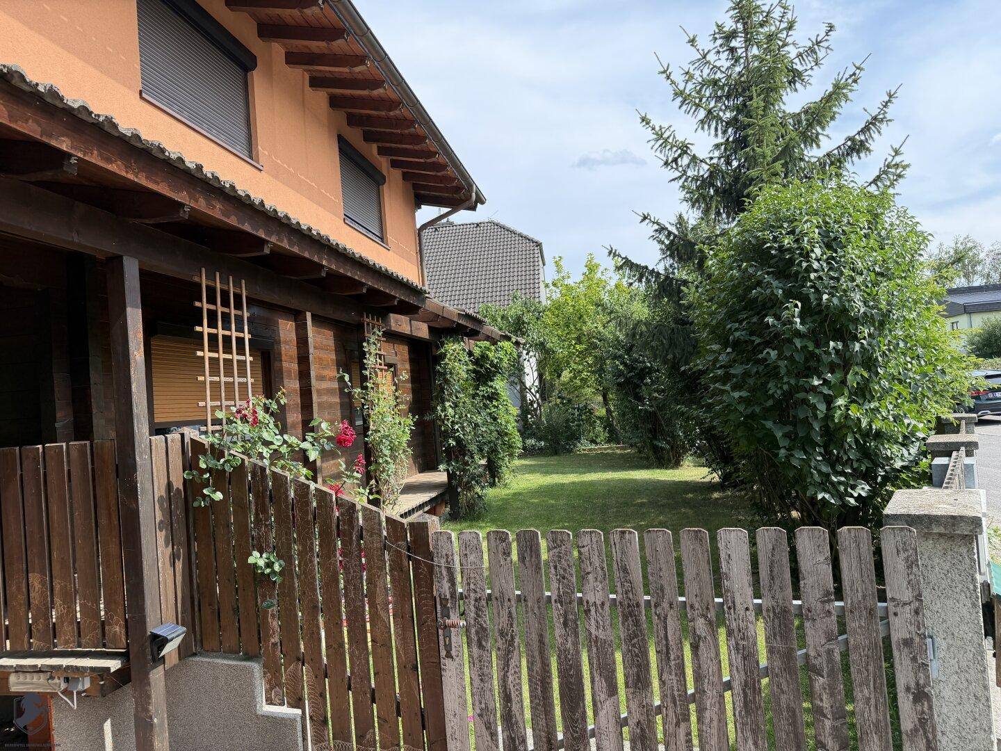 Seitenansicht des Hauses mit Gartenbereich, Rasenfläche und blühenden Rosensträuchern am Zaun.