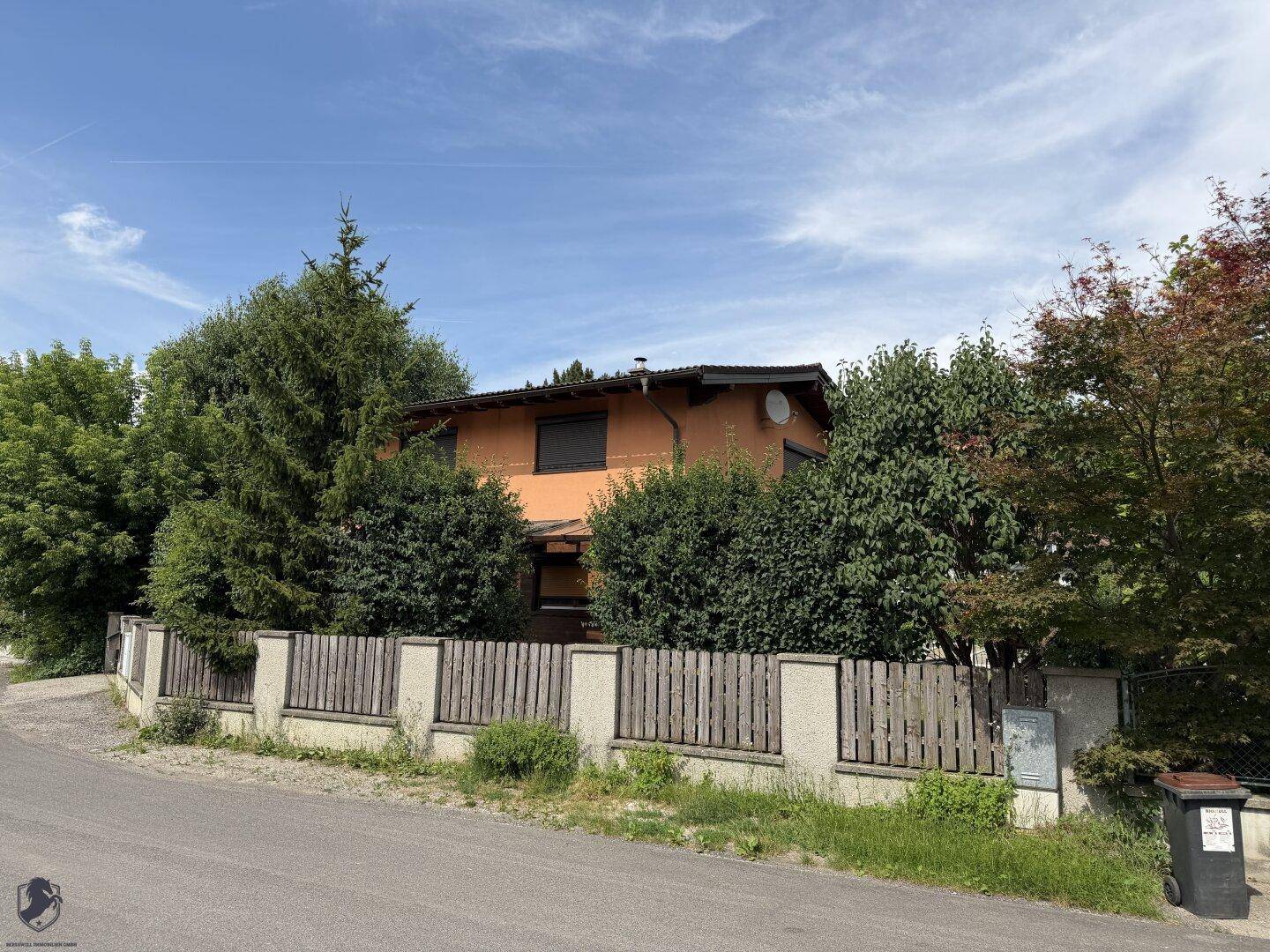 Weitläufige Außenansicht des Hauses mit üppiger Bepflanzung und einem klaren blauen Himmel.