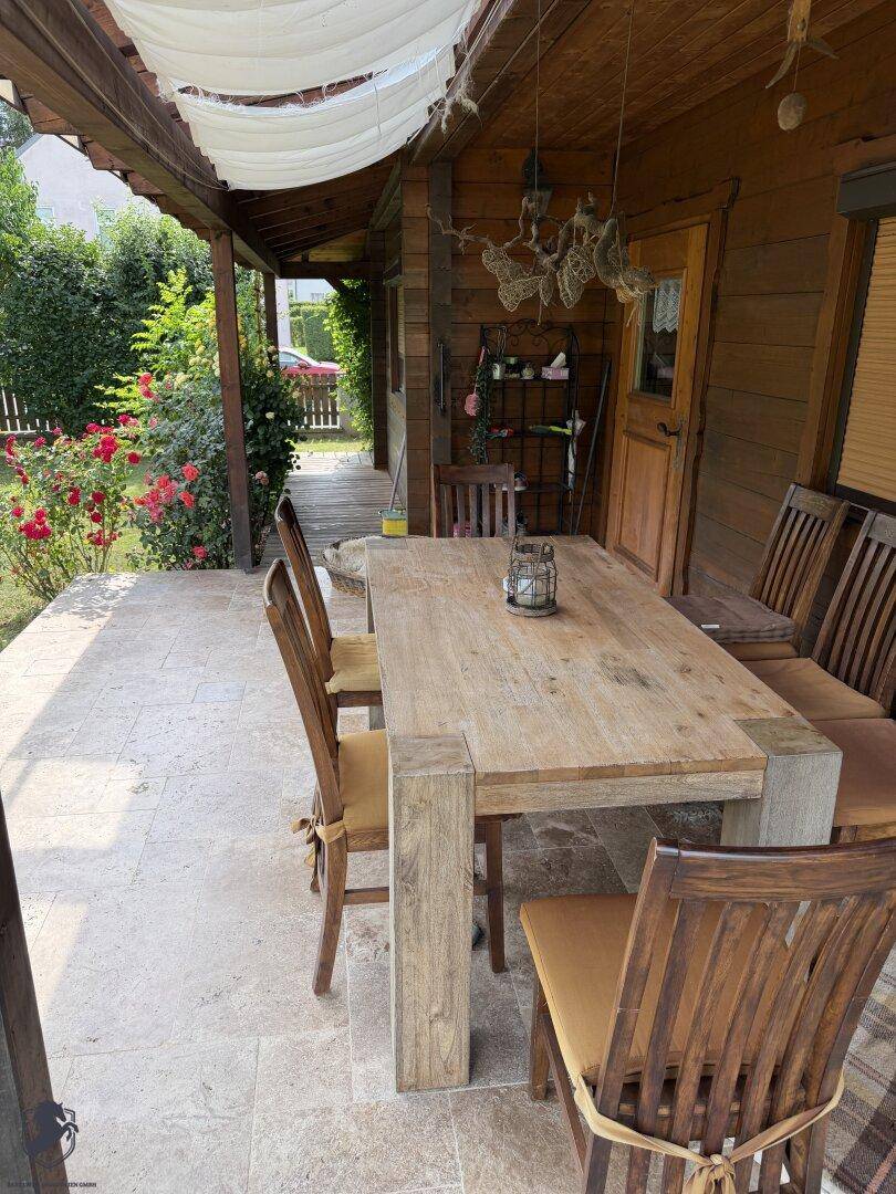 Überdachte Terrasse mit Holztisch und Stühlen, ideal für Mahlzeiten im Freien, mit Fliesenboden.
