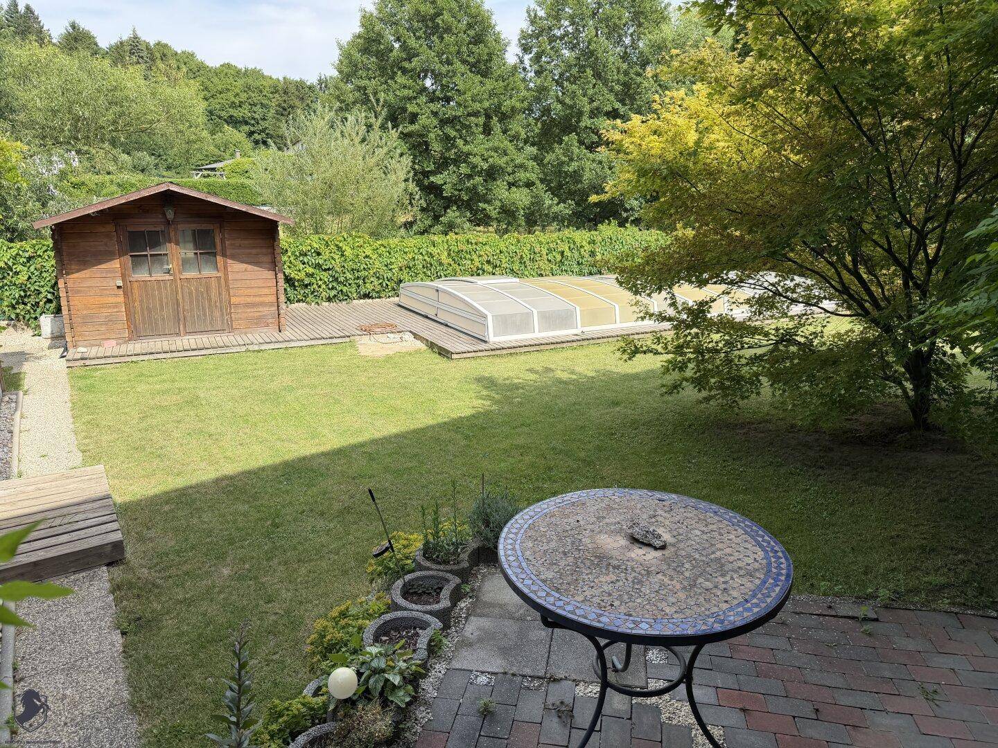 Gartenansicht mit Poolabdeckung, Holzschuppen und einem kleinen runden Tisch im Vordergrund.