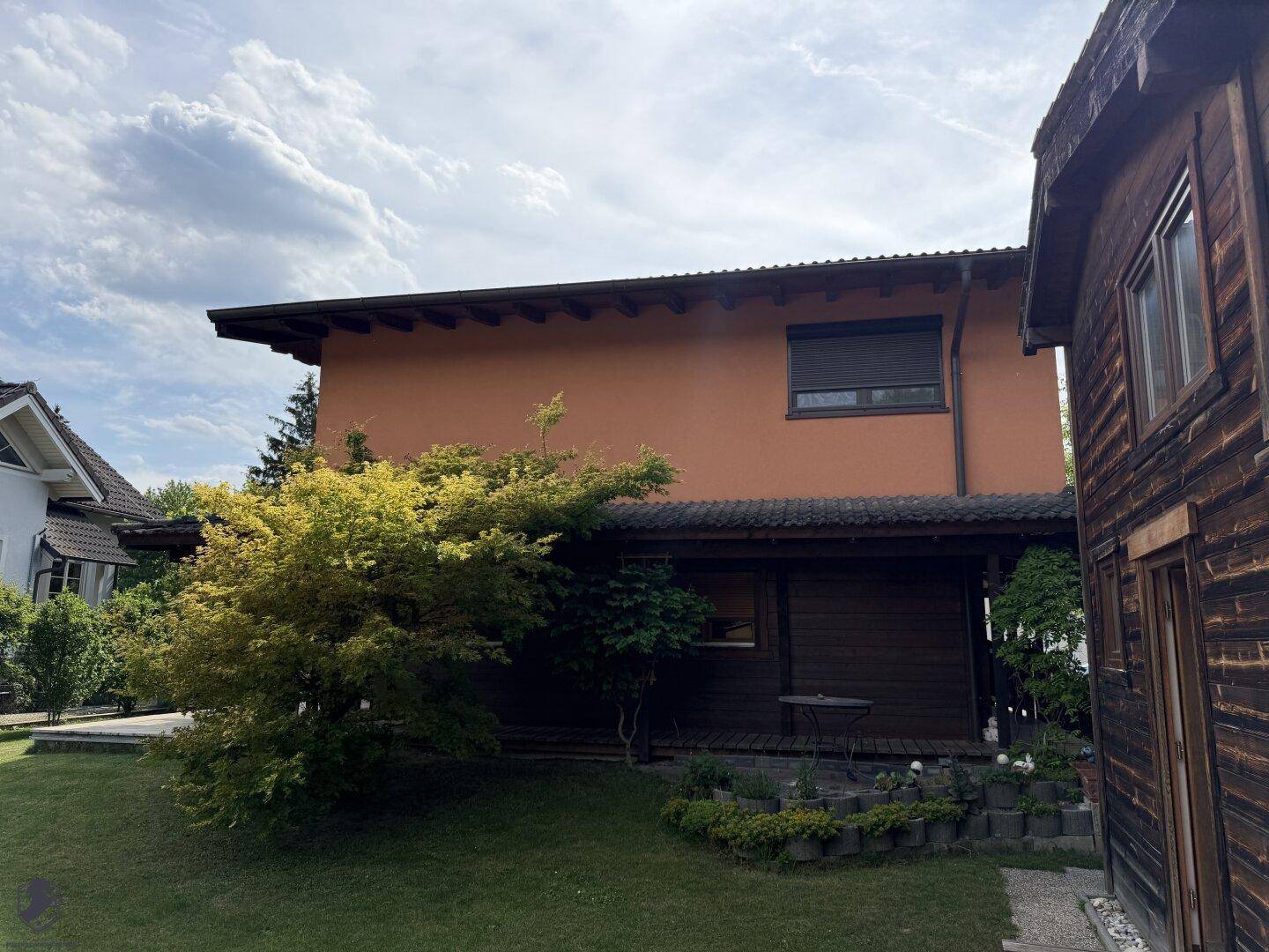 Seitenansicht des Hauses mit Garten, Rasenfläche und einem kleinen Baum im Vordergrund.