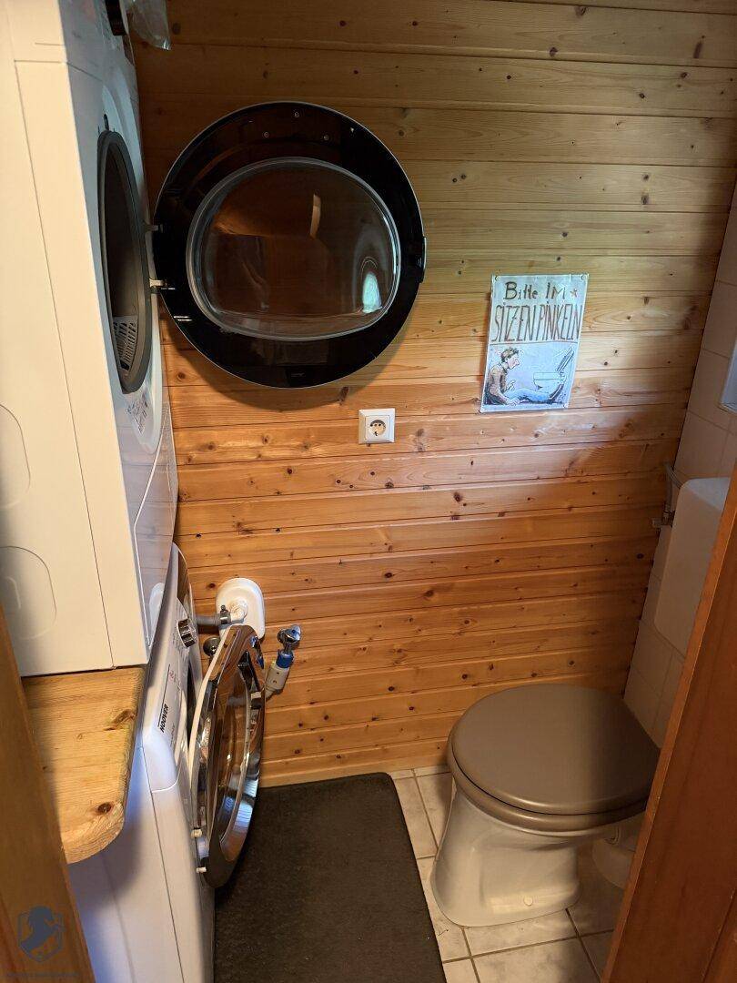 Kleines WC mit Holzvertäfelung, Waschmaschine und Trockner, sowie einem Fenster.