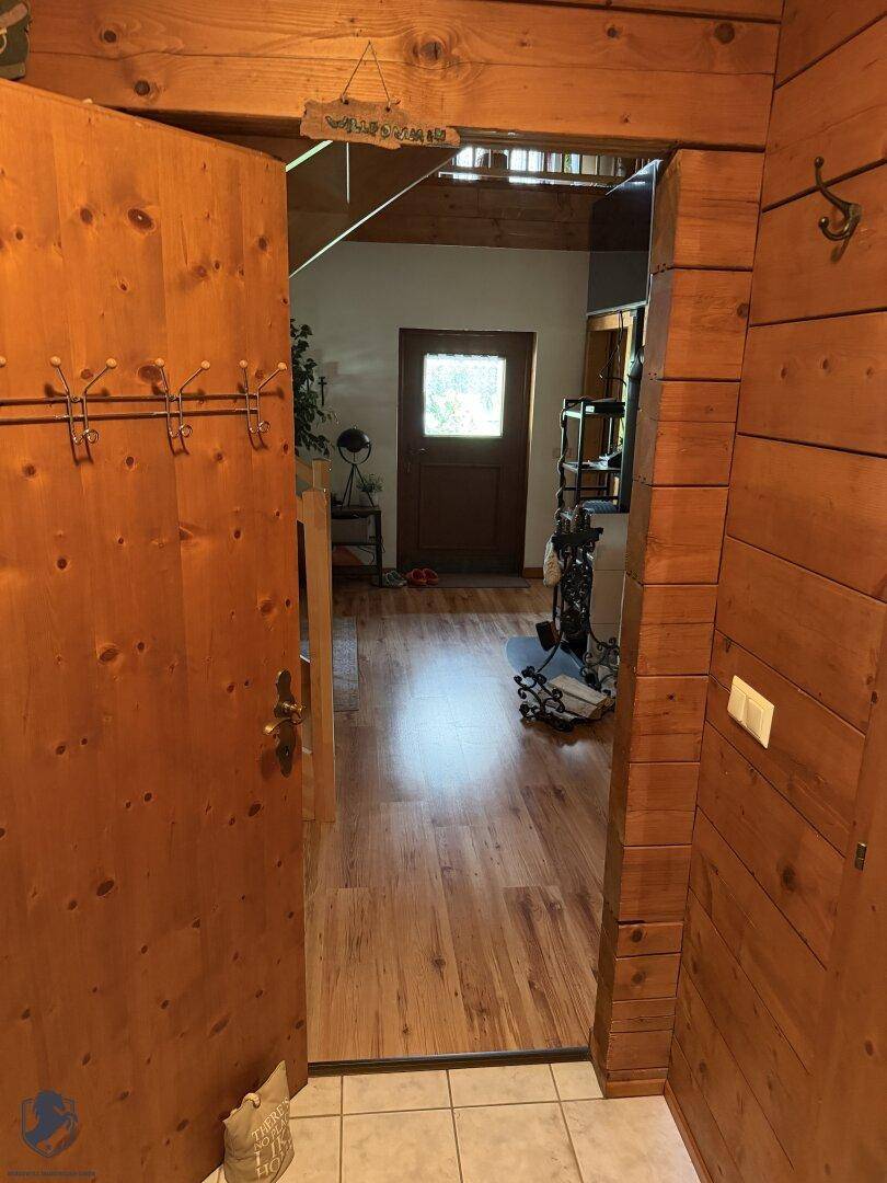 Eingangsbereich mit Holztür, Garderobe und Laminatboden, der in den Wohnbereich führt.