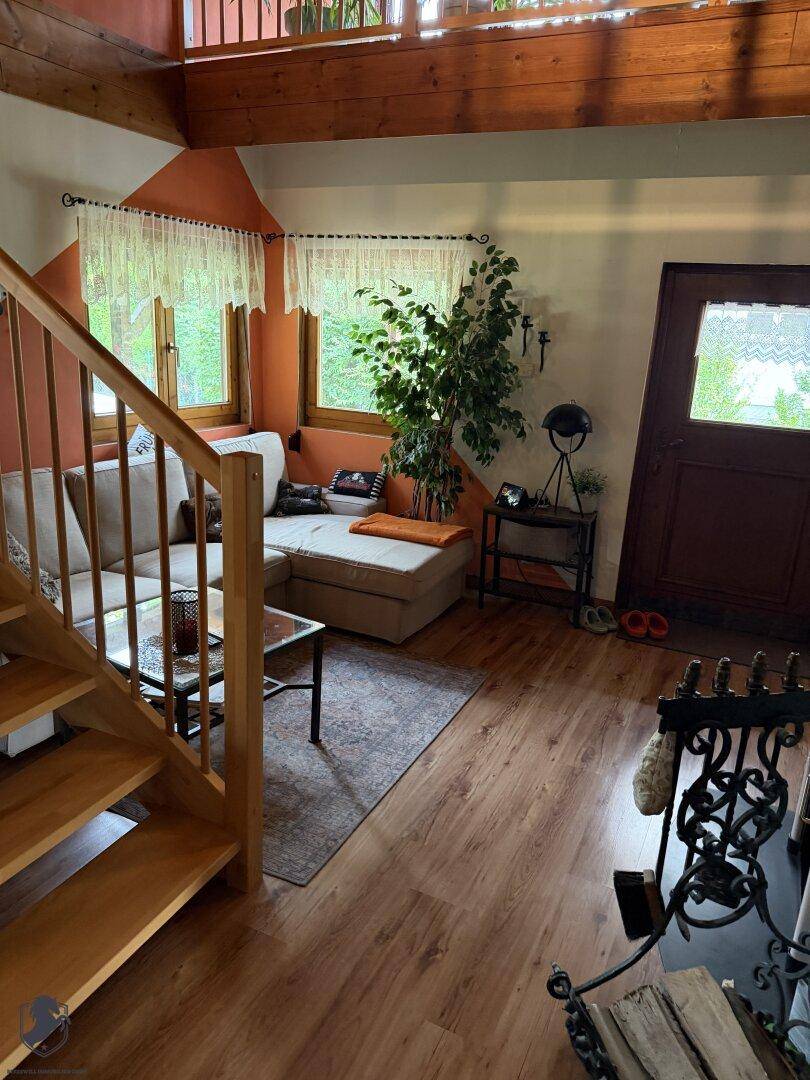 Heller Wohnbereich mit Sofa, Holzboden und Treppe zum oberen Stockwerk, mit Kaminofen.