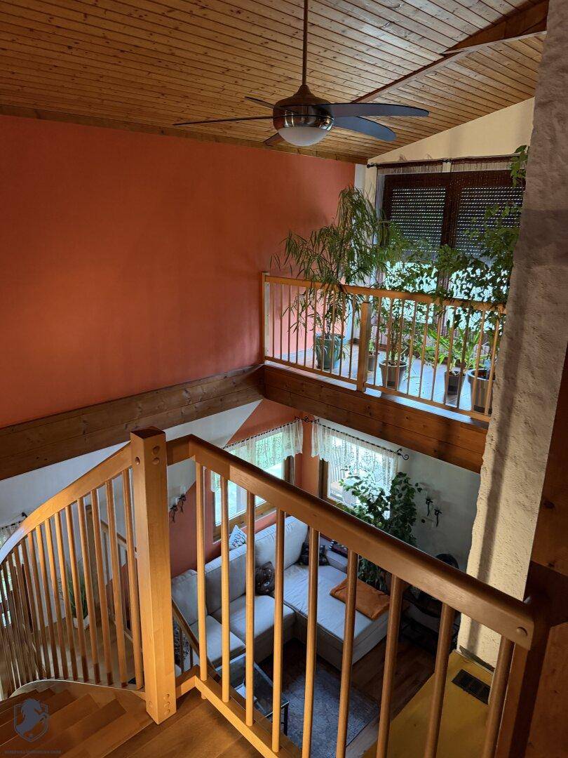 Wohnzimmer mit Holztreppe, hoher Decke und Deckenventilator, der für angenehme Luft sorgt.