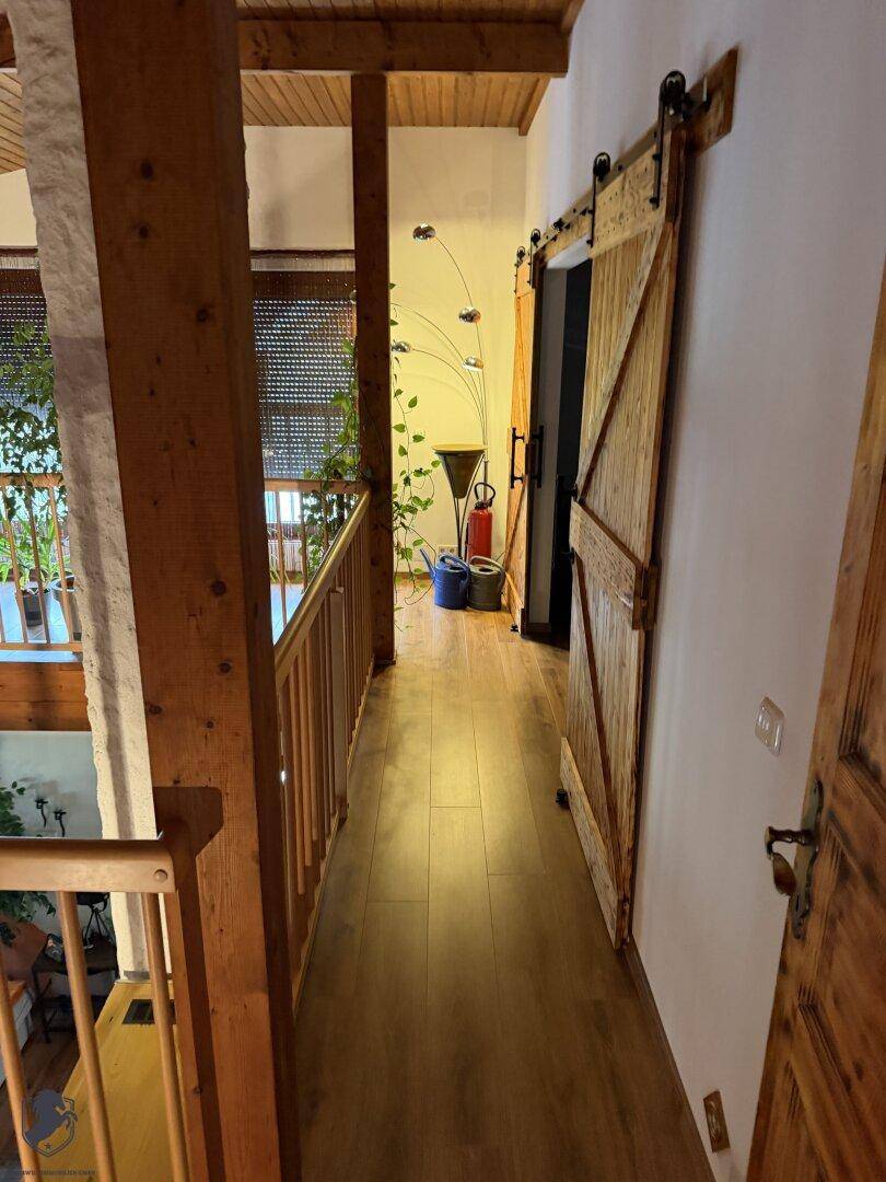 Flur auf der oberen Etage mit Holzboden und einer rustikalen Schiebetür, die zu einem Zimmer führt.