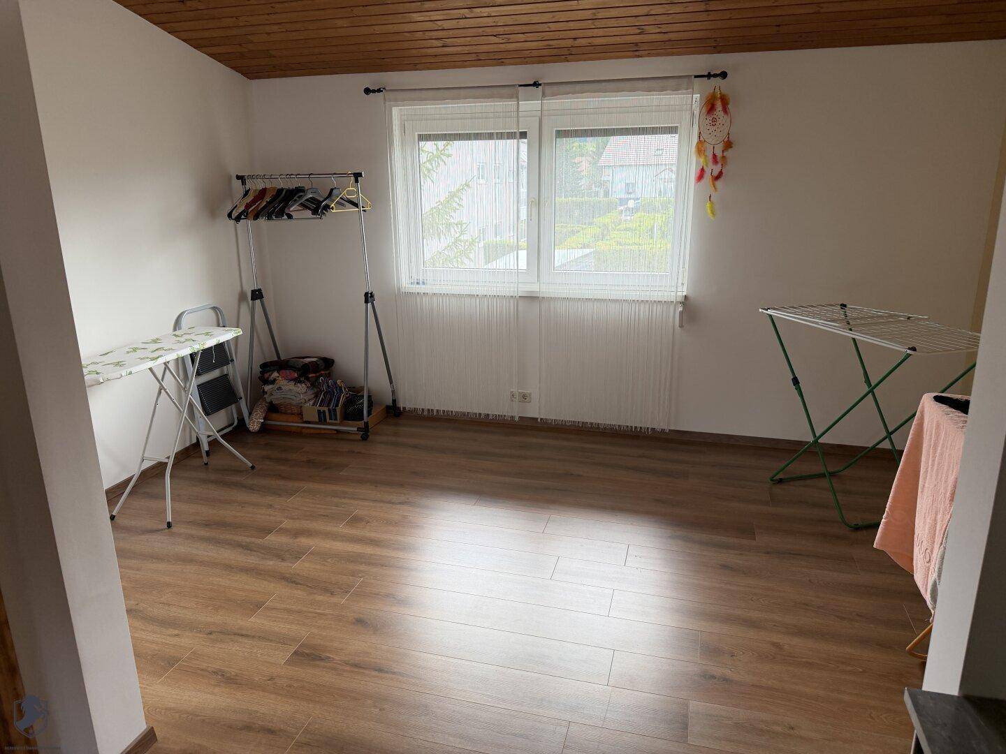 Heller Raum mit Holzdecke und Laminatboden, ausgestattet mit Wäscheständern und Bügelbrett.