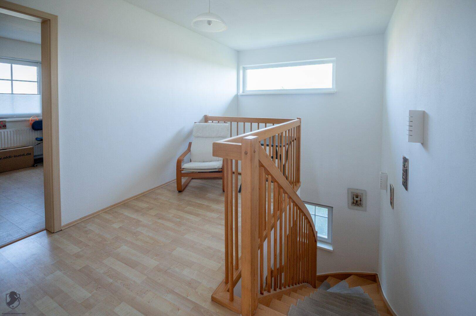 Oberer Flurbereich mit Holztreppe und hellem Laminatboden, der zu weiteren Zimmern führt.