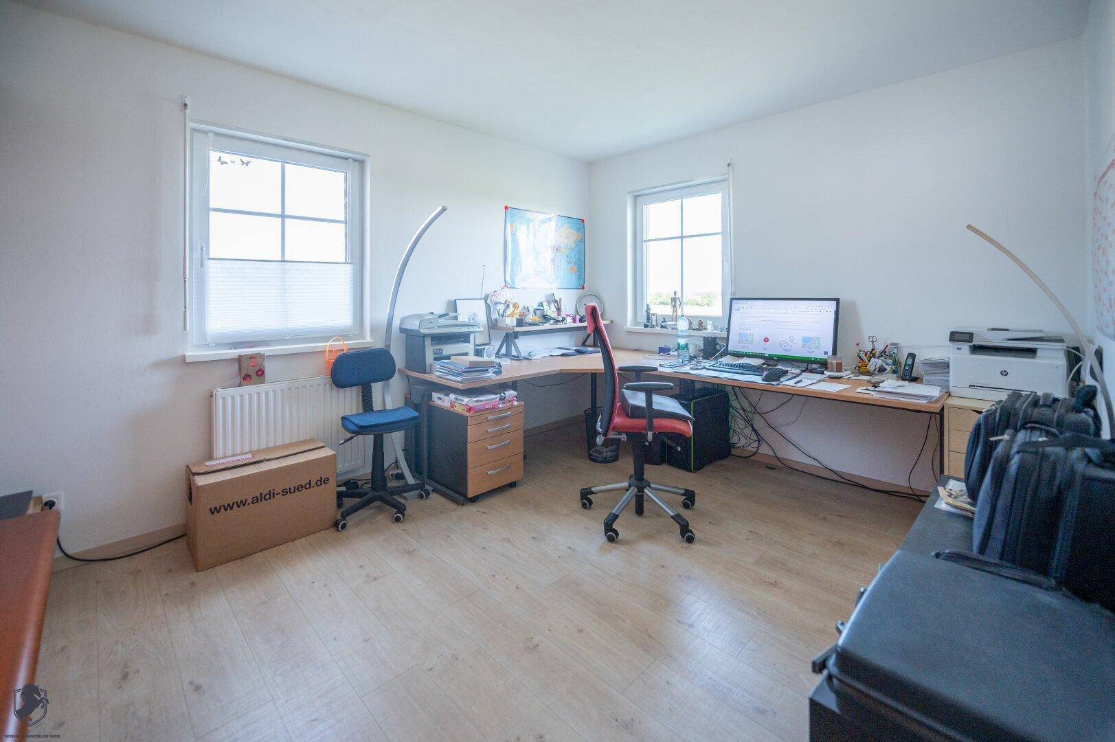 Helles Arbeitszimmer mit zwei Fenstern, Schreibtisch und Laminatboden, ideal für Home-Office.