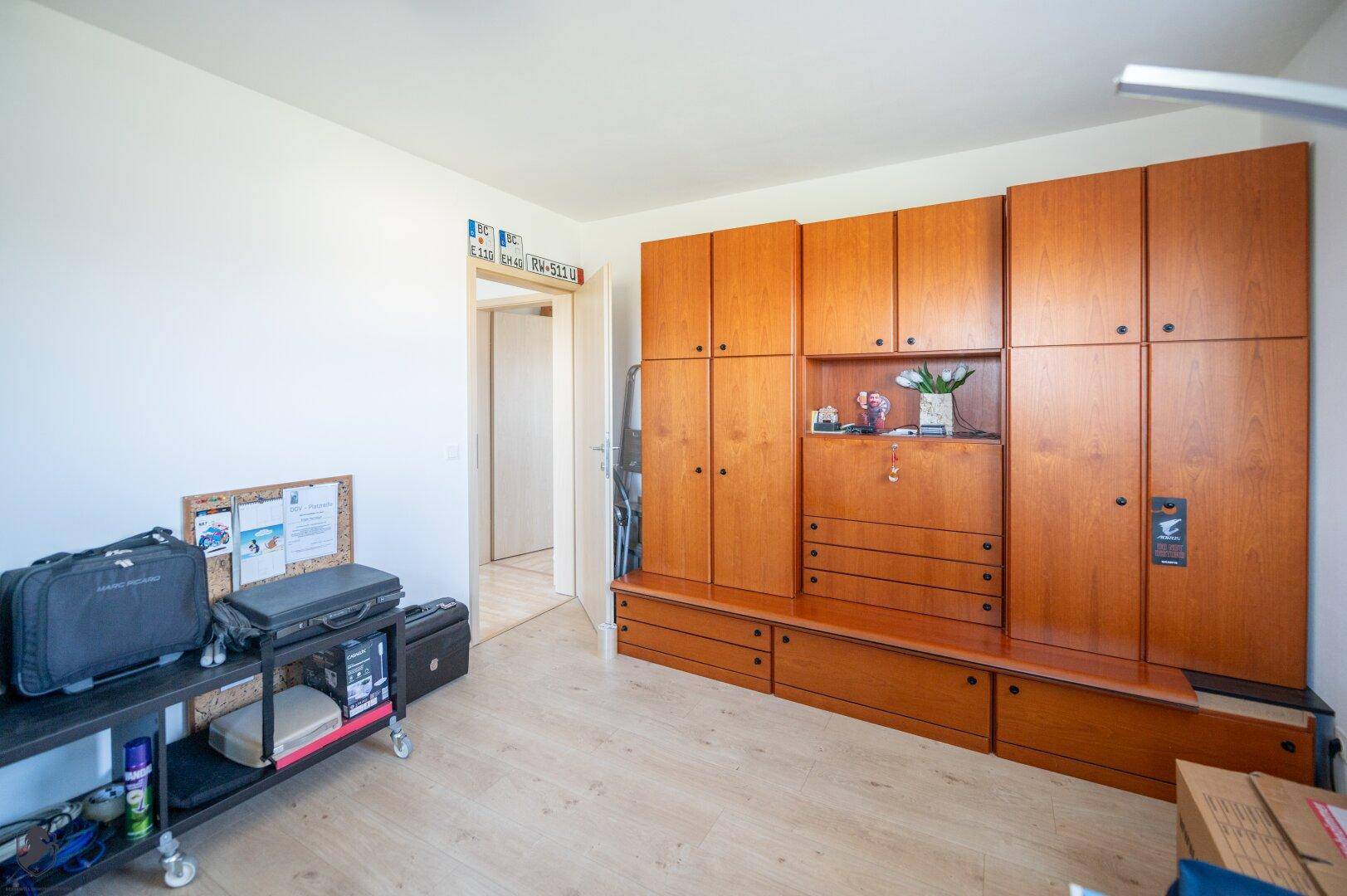 Zimmer mit großem Holzschrank und Laminatboden, bietet viel Stauraum und Zugang zu weiteren Räumen.