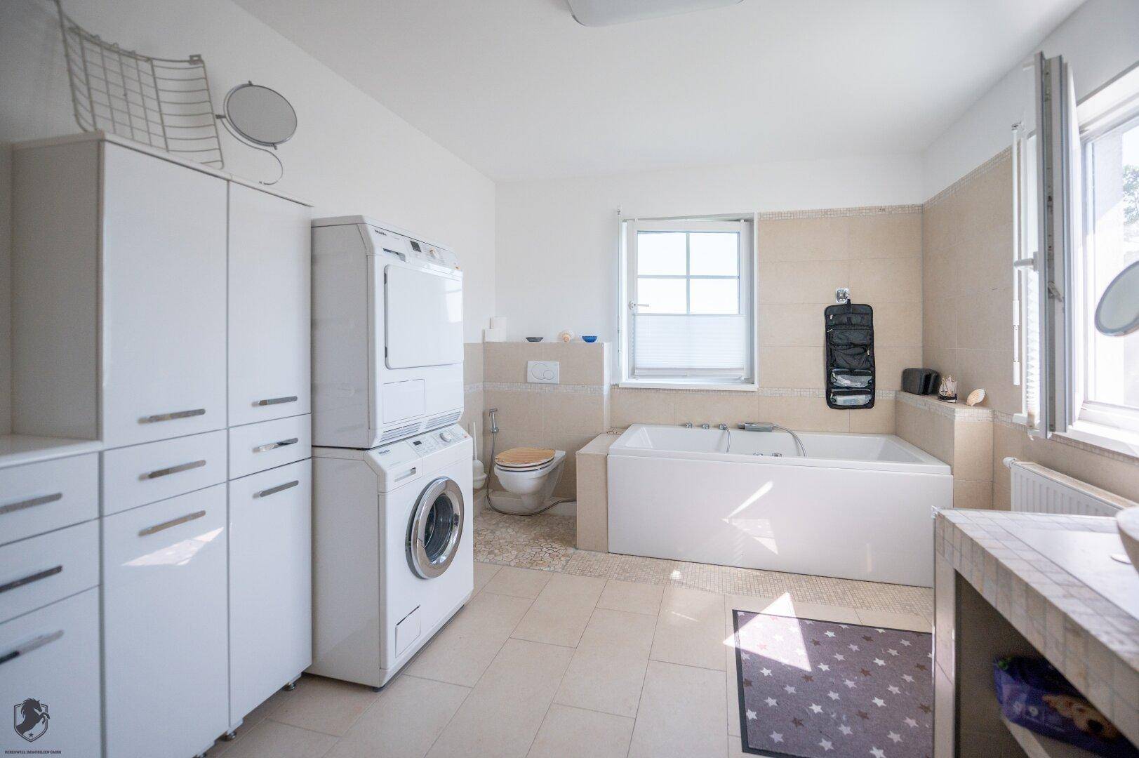 Helles Badezimmer mit Waschmaschine und Trockner, Badewanne und WC, praktisch und funktional.