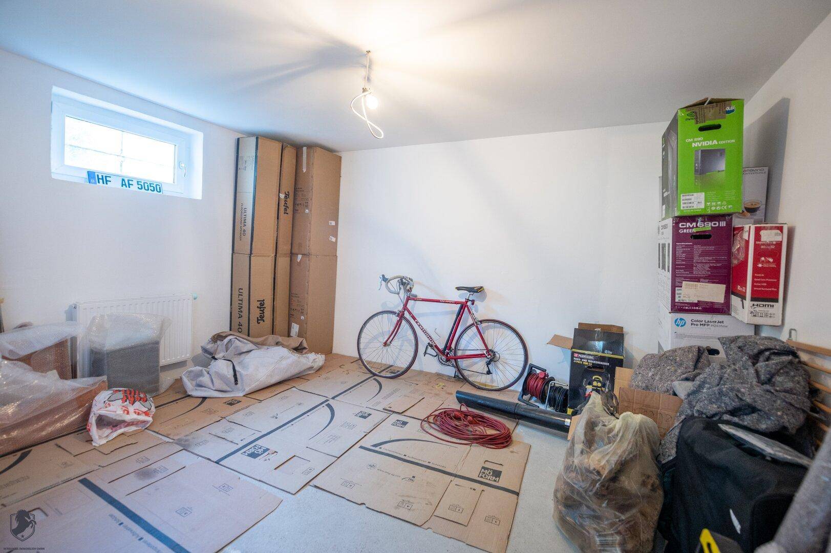 Kellerraum mit Fahrrad und Kartons, bietet zusätzlichen Stauraum und ein kleines Fenster.