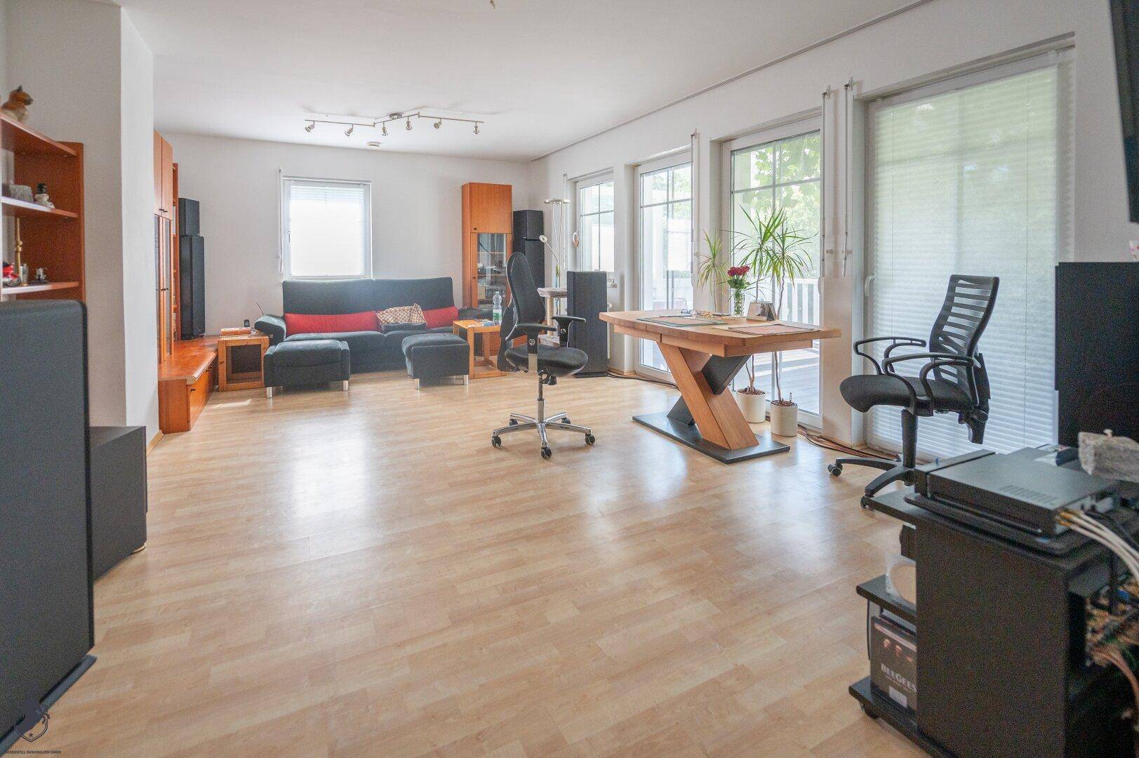 Geräumiges Wohnzimmer mit hellem Laminatboden, großen Fenstern und Zugang zur Terrasse.