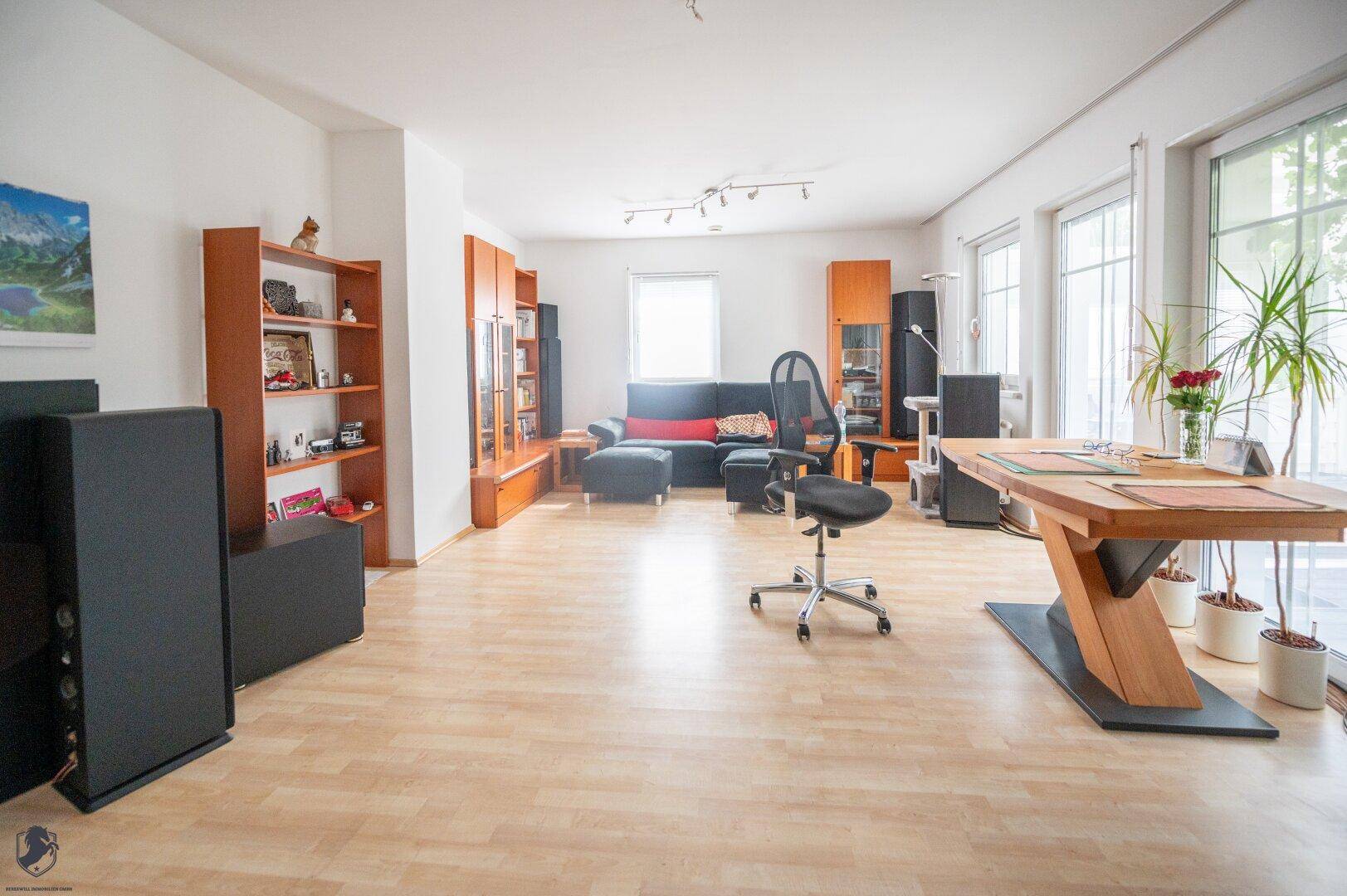 Helles Wohnzimmer mit Laminatboden, bequemer Sitzecke und viel Tageslicht durch große Fenster.