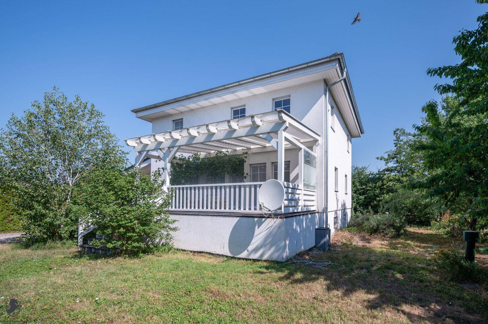 Rückseite des Hauses mit großer Terrasse, Pergola und angrenzendem Gartenbereich.