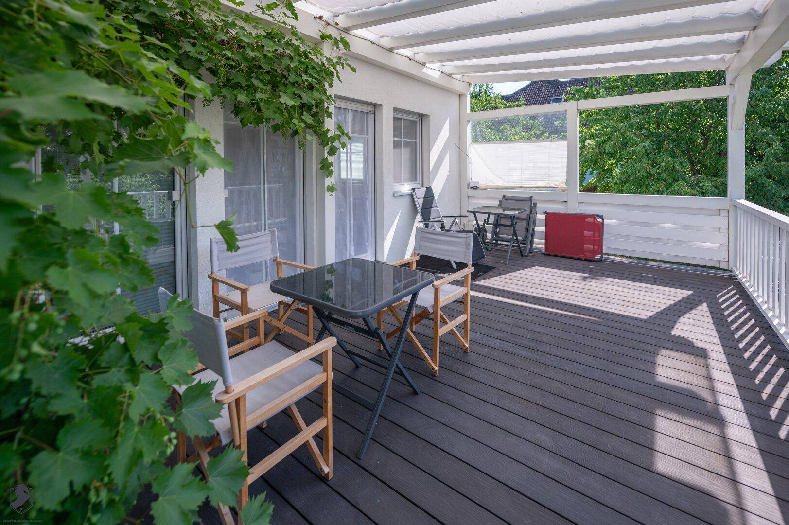 Gemütliche Terrasse mit dunklem Holzboden, Pergola und Sitzgelegenheiten im Grünen.