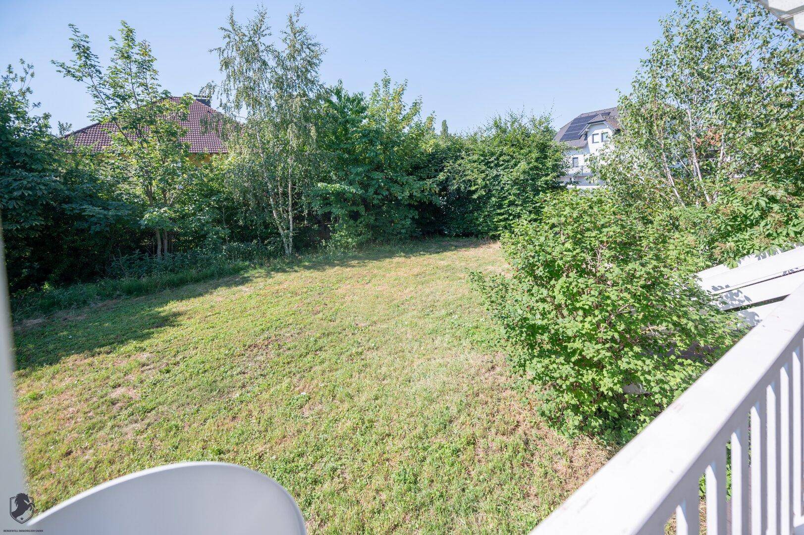 Großer Gartenbereich mit viel Grün, Bäumen und einer schützenden Hecke im Hintergrund.