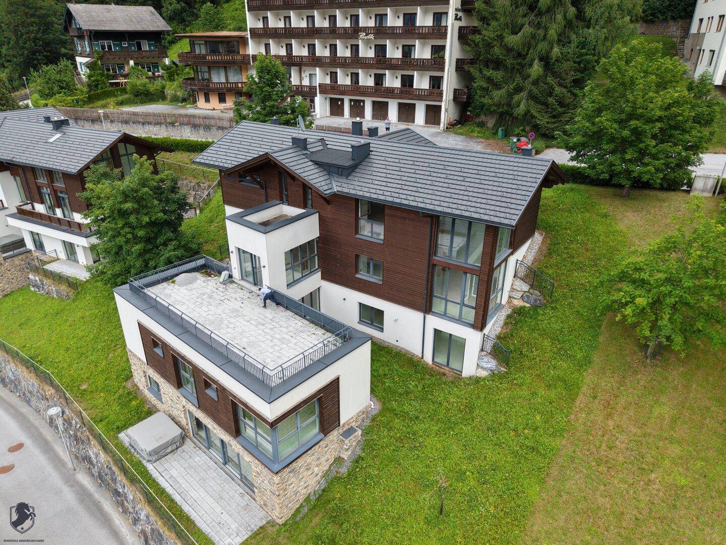 Luftaufnahme von mehreren modernen Häusern mit dunklen Dächern und großen Fenstern in einer Hanglage.