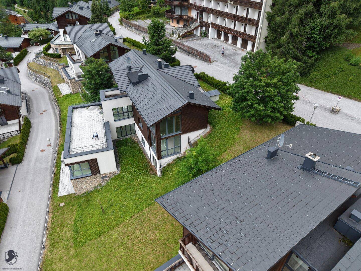 Panoramablick auf eine moderne Wohnsiedlung mit Häusern in Hanglage und weitreichender Berglandschaft.