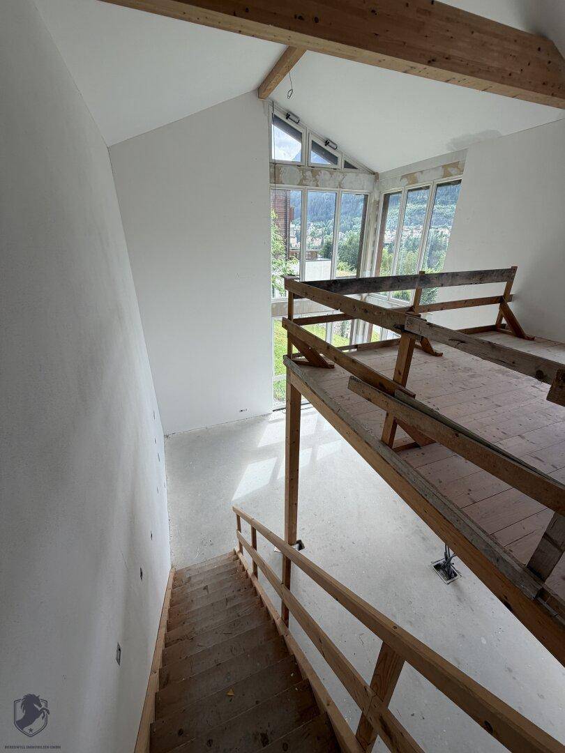 Heller Raum mit hohen Decken, Holzbalken und großen Fenstern, die einen weiten Blick auf die Berge bieten.