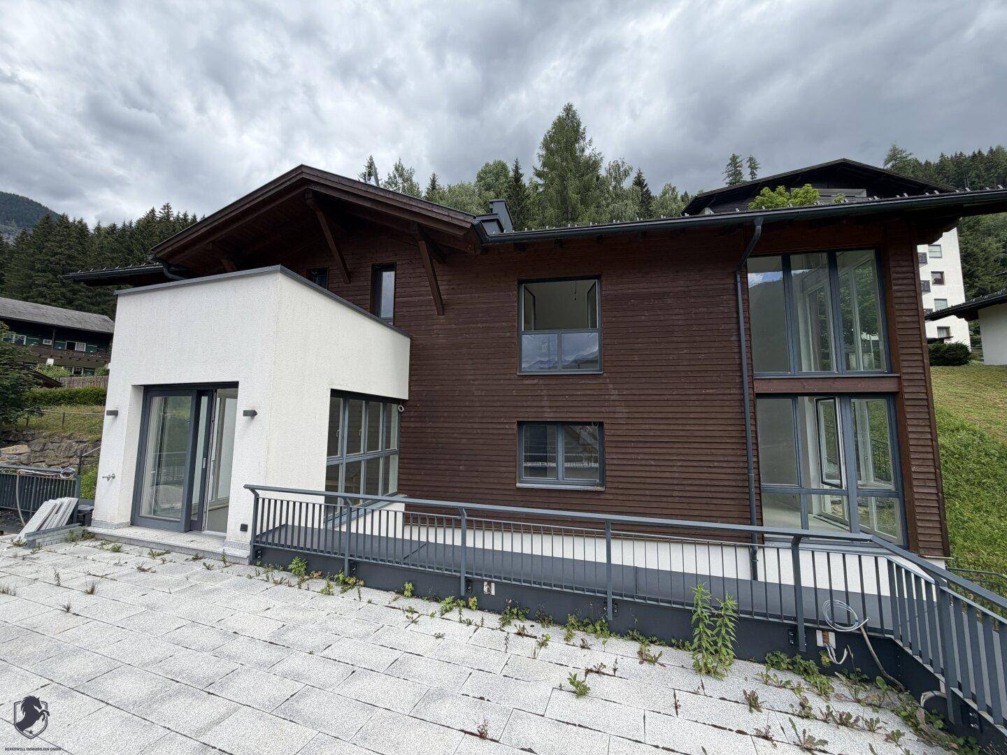 Moderne Hausfassade mit Holzverkleidung, weißen Akzenten und großen Fensterfronten in Hanglage.