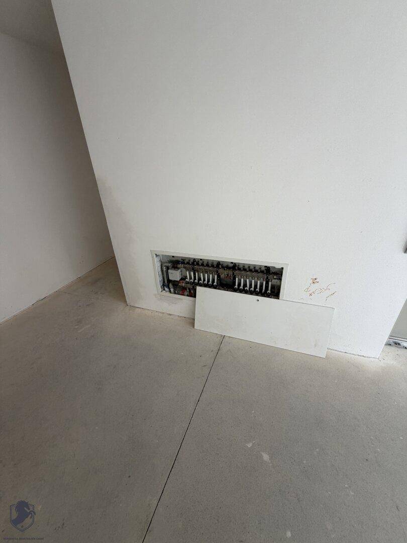 Offener Elektroschaltkasten in einem unfertigen Raum mit weiß gestrichenen Wänden.