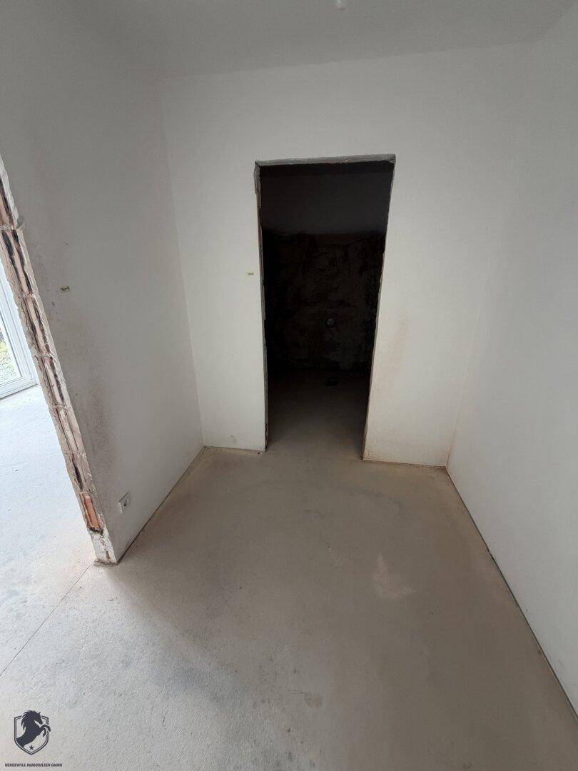 Unfertiger Raum mit weiß gestrichenen Wänden und einem dunklen Türrahmen, bereit für den Ausbau.