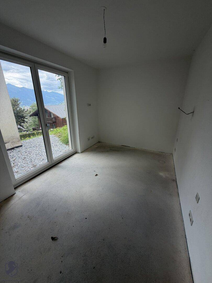 Unfertiger Raum mit großer Glasschiebetür und Blick auf die grüne Umgebung.