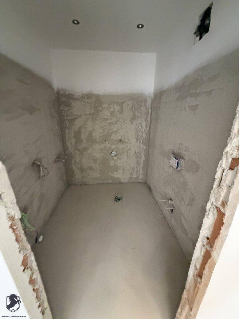 Unfertiges Badezimmer mit vorbereiteten Anschlüssen und rauen Wänden, bereit für den Ausbau.