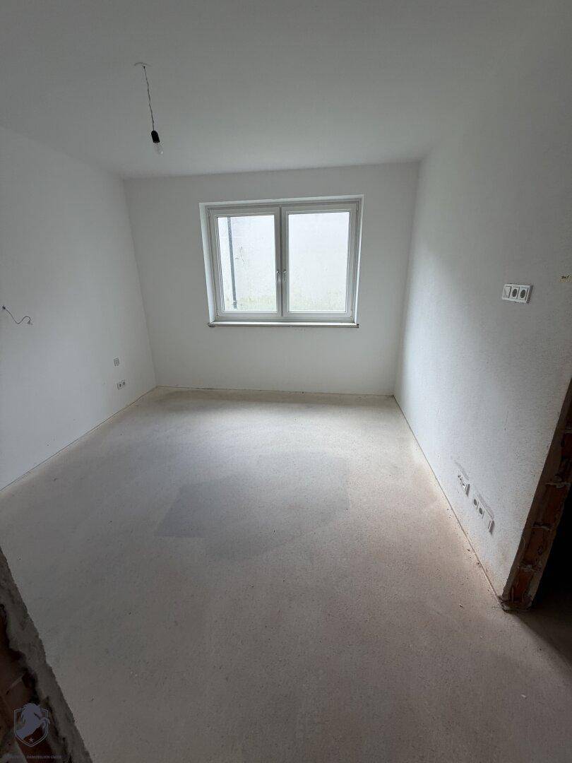Unfertiger Raum mit einem Fenster und Betonboden, bereit für den weiteren Ausbau.
