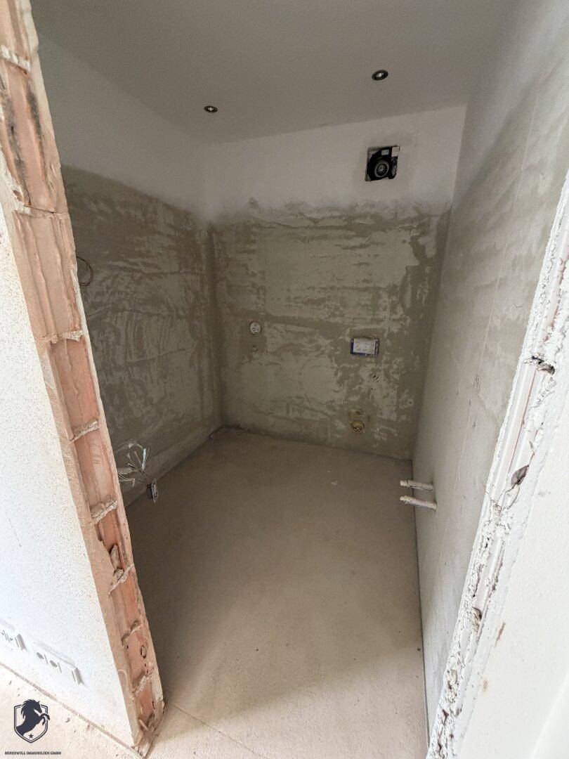 Unfertiges Badezimmer mit vorbereiteten Anschlüssen und rauen Wänden, bereit für den Ausbau.