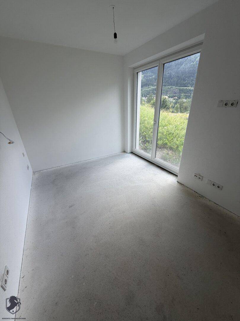 Unfertiger Raum mit großer Fensterfront und Betonboden, bereit für den Ausbau.