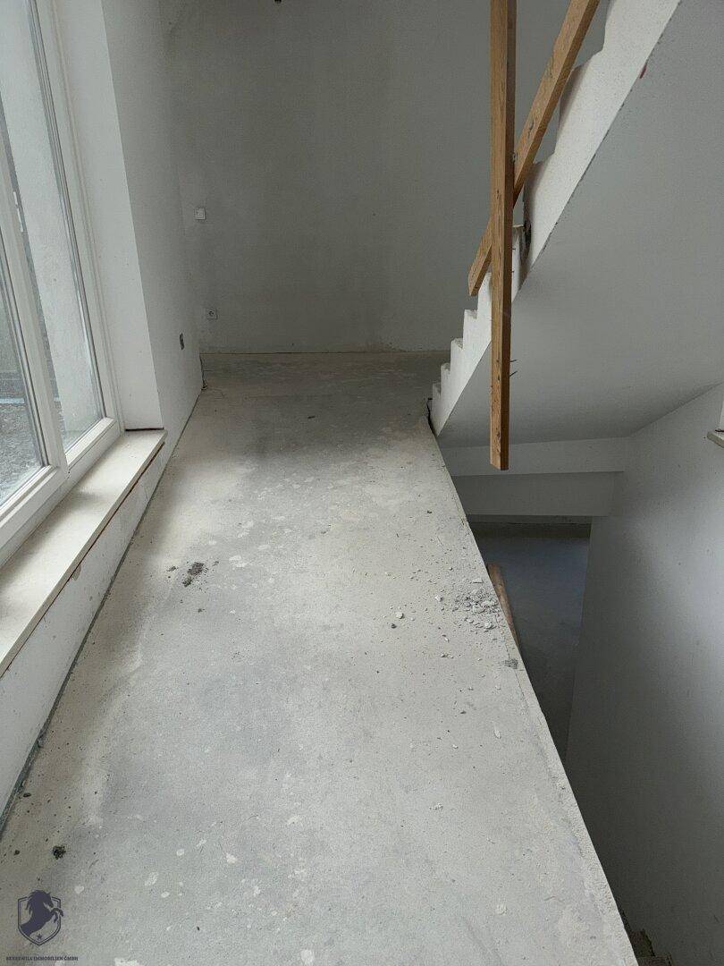 Unfertiger Innenbereich mit Rampe, Treppe und großen Fenstern, bereit für den Ausbau.