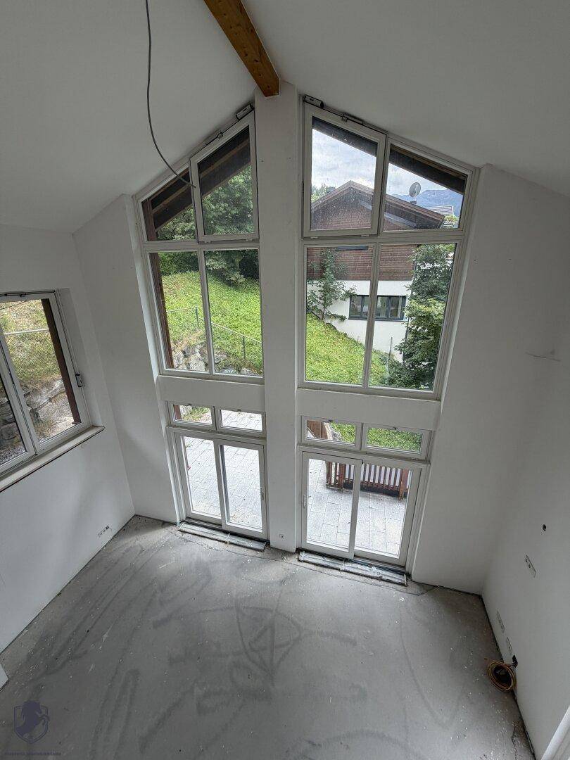 Lichtdurchfluteter Wohnraum im Rohbau mit hohen Fenstern und Blick auf die Natur, offenes Design.