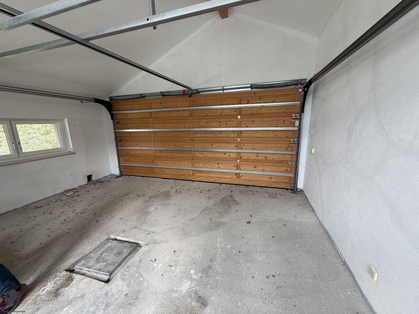 Unfertige Garage mit Holz-Garagentor und Fenster, bereit für die Fertigstellung und Nutzung.