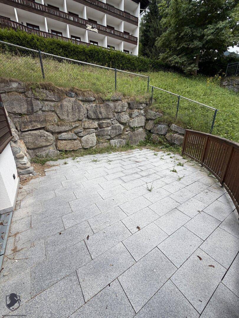 Gepflasterte Terrasse mit Steinmauer und Blick auf die umliegende Vegetation, ideal für Entspannung.