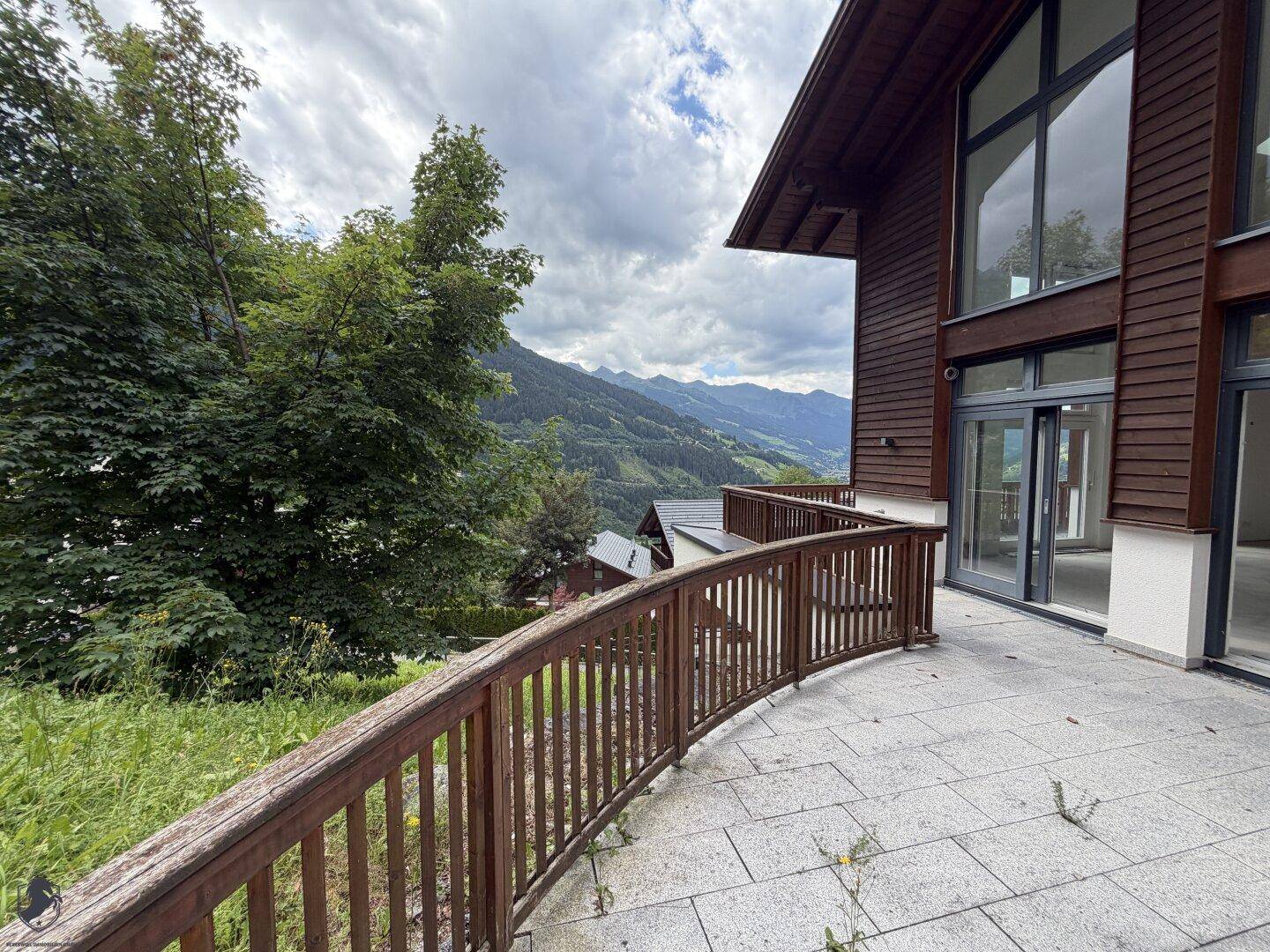 Große Terrasse mit Holzgeländer und weitem Blick auf die Berglandschaft unter bewölktem Himmel.