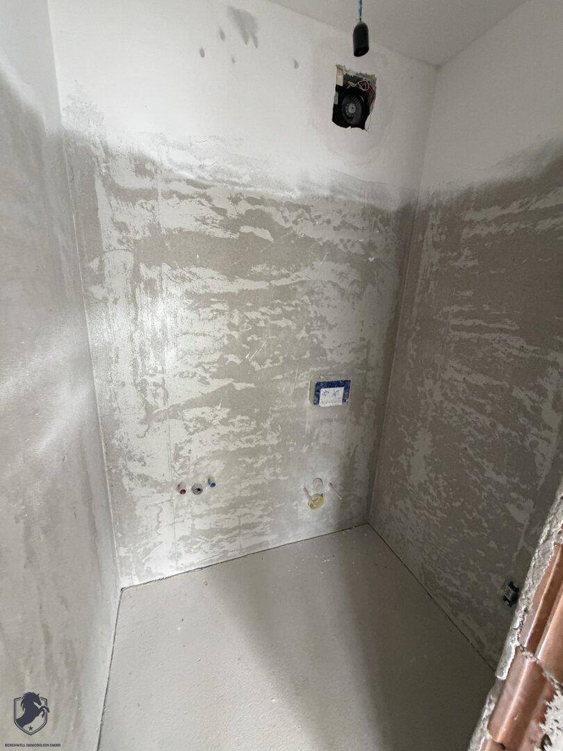 Unfertiger kleiner Raum mit vorbereiteten Anschlüssen für ein Badezimmer oder WC, im Rohbau.