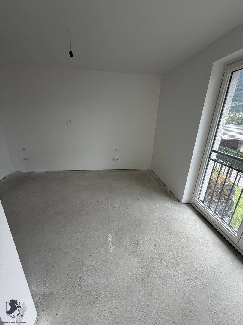 Leerer Raum im Rohbau mit Betonboden und Zugang zu einem französischen Balkon.