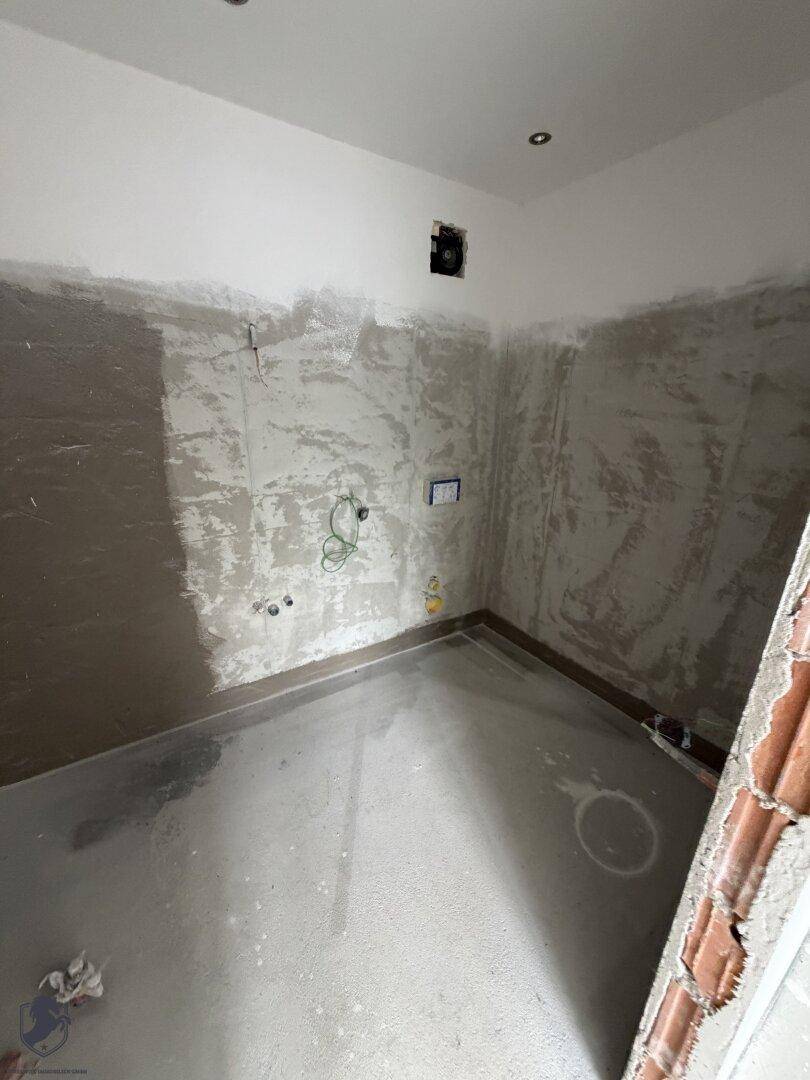 Raum im Rohbau mit sichtbaren Installationen und vorbereiteten Wänden für den Ausbau.