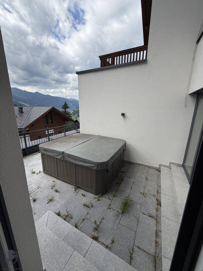Außenterrasse mit Whirlpool und Fliesenboden, umgeben von einer malerischen Berglandschaft.