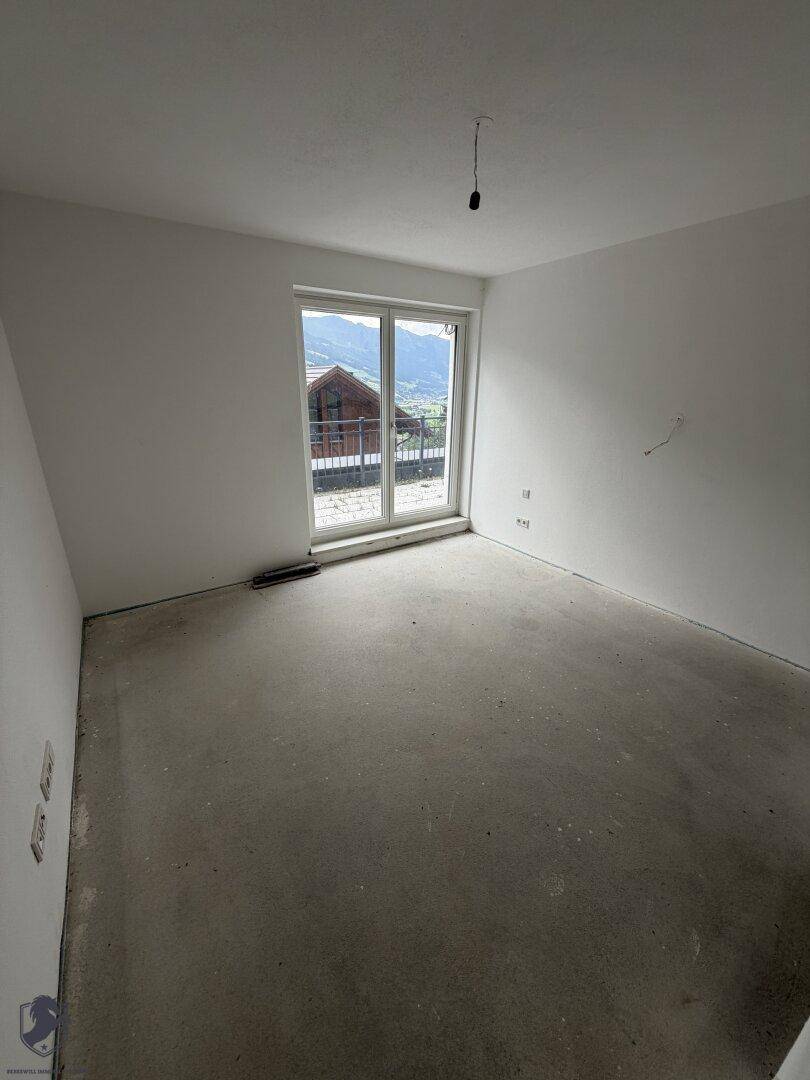 Unfertiger Raum mit Betonboden und einem großen Fenster, das einen Blick auf die Umgebung bietet.